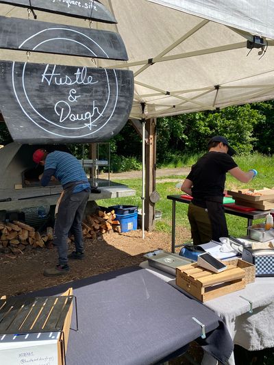 Two cooks preparing pizza in front of an outdoor oven, Bilston Farm