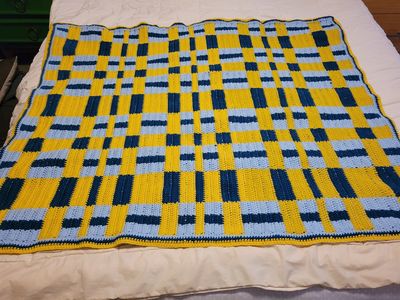 my new gift blanket, laid across our bed. Blocks of baby blue, dark blue and golden yellow sections made to look like thick woven bands